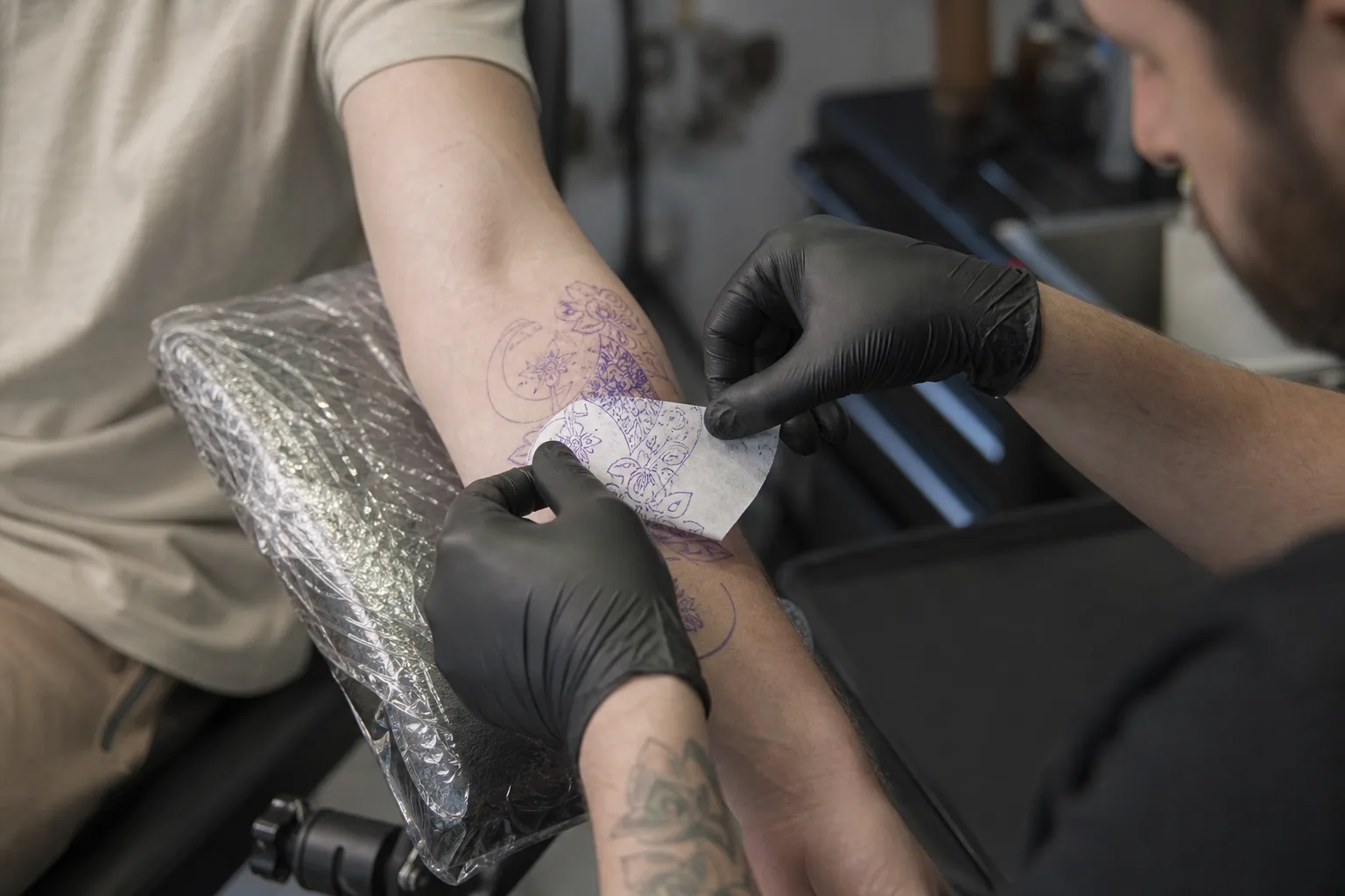 Tattoo artist preparing stencil transfer paper on a client forearm